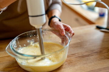 Mixing Creamy Batter Using Handheld Blender in Cozy Kitchen During Sunny Afternoon