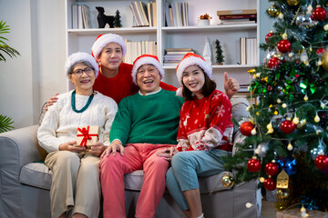 Asian family on Christmas Day. Everyone is happy together in a Christmas themed room filled with presents and orange lights.