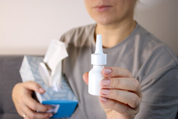 Fototapeta premium Close up of sick woman holing white nose spray bottle, blurry background 