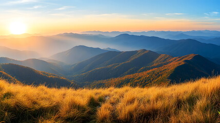 Obraz premium Landscape of majestic mountain ranges at sunrise, with golden sunlight casting soft rays over distant hills and valleys. The foreground consists of a grassy ridge covered in golden autumn hues.
