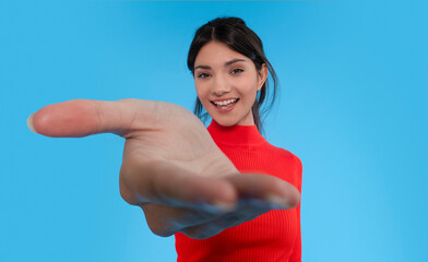 Smiling Young Woman Extends Her Hand in Greeting Against Bright Blue Background