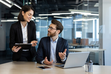 Colleagues engaged in discussion in modern office with laptop table. Woman holding documents, man...