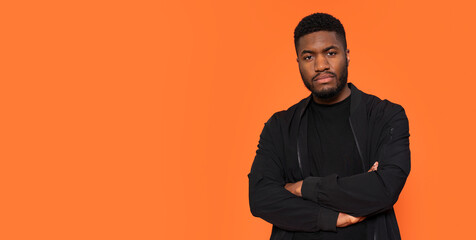 Confident Young Man Poses Against Vibrant Orange Backdrop Showcasing Modern Style and Attitude