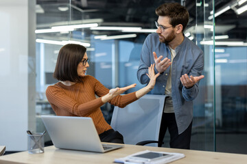 Office workers experiencing conflict at workplace illustrating concept of workplace disagreement. Focus on heated argument between man and woman in professional environment with laptop on desk.