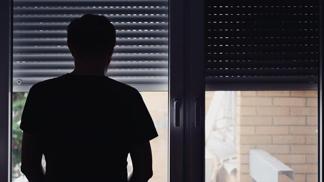 Silhouette of depressed sad man in dark room with window shutters pulled down