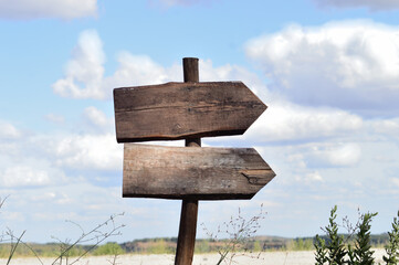 Hand-cut wooden arrows nailed to a stick stuck in the ground, without inscriptions, cloudy sky in the background, open air, signs