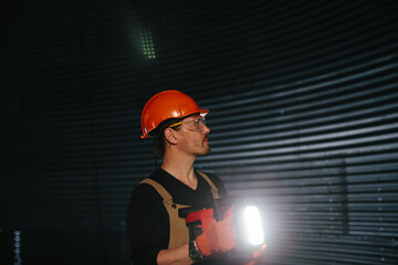Male worker in safety helmet with flashlight in hands inside storage tank. Inside the grain silo.