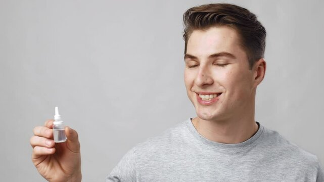 Medicine and pharmacy. Studio portrait of young man holding bottle with medical drops and smiling to camera, grey background, slow motion