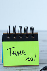 Thank you, handwritten quote on green paper note placed on wooden desk with white background....