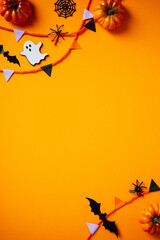 Halloween holiday flat lay composition with paper garland, decorations, bats, ghosts, spiders on orange background. Halloween vertical banner design, poster template