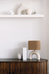 Modern minimalist decor on wooden sideboard with lamp and art pieces in bright room
