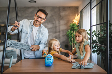Father and daughters wipe dust from the table at home