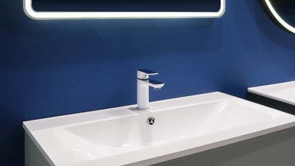 A white sink with a chrome faucet and a blue wall behind it. The sink is clean and shiny, and the blue wall adds a pop of color to the room