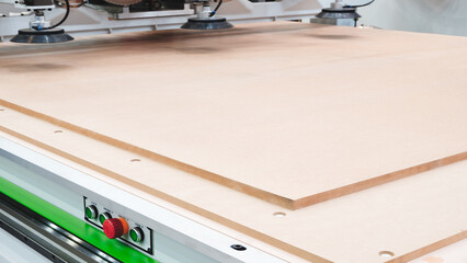 A woodworking shop with a large machine cutting a piece of wood. The machine is surrounded by a lot...