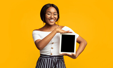 Smiling Black Girl Showing Digital Tablet Blank Screen Standing Over Orange Studio Background. Great Application Concept. Mockup