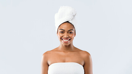 Portrait of happy young black woman wrapped in bath towels over grey studio background