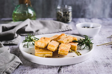 Spicy fried tofu on skewers and rosemary on a plate on the table