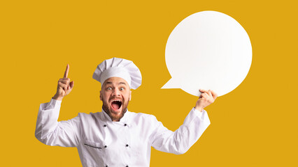 Recipe Idea. Excited Chef Man Holding Blank White Speech Bubble Pointing Finger Standing On Black Studio Background. Panorama, Mockup