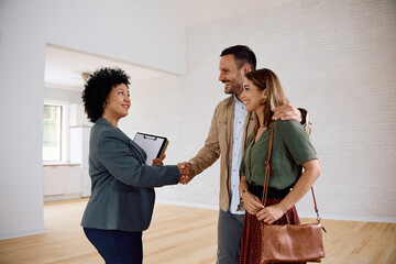 Happy couple and their real estate agent shaking hands in new house.