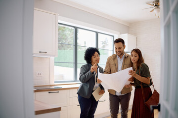 Young couple examining housing plans with real estate agent while standing in  kitchen.