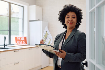Happy agent examining housing plans of  real estate for sale and looking at camera.