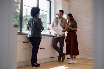 Happy couple of property buyers analyzing housing plans with their real estate agent.