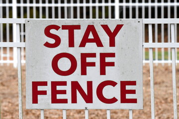 A red and white sign attached to a fence that has red letters that say "Stay off Fence".