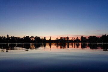 Naklejka premium Sunset on the lake with trees in silhouette and blue red sky.