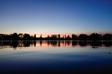 Naklejka premium Sunset on the lake with trees in silhouette and blue red sky.