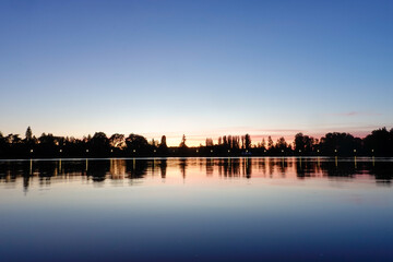 Sunset on the lake with trees in silhouette and blue red sky.