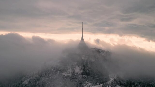 Experience the breathtaking ascent of Jested Mountain in Liberec, Czechia, as thick clouds envelop its iconic tower, creating a mystical atmosphere and showcasing nature's beauty.