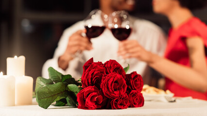 Romantic Date Concept. Bouquet Of Red Roses Lying On Restaurant Table, Unrecognizable Couple Clinking Glasses Celebrating Valentine's Day. Panorama, Cropped