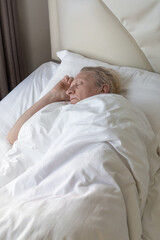 Sleeping mature man on a bed with white linen in his bedroom. Comfortable Rest and relaxation.