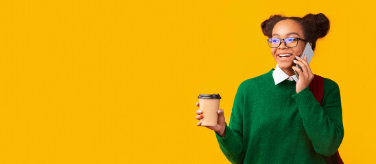 Always In Touch. Happy afro teenager talking on mobile phone drinking coffee, looking at copypace, panorama