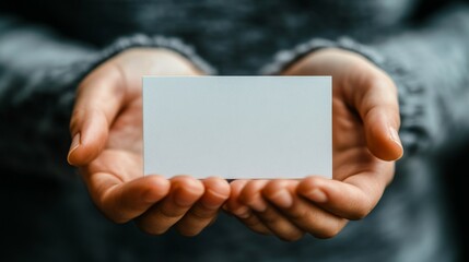 Person holding a blank business card in hands with a soft background during daylight