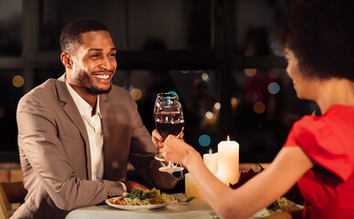 Romantic Date Concept. Loving Afro Spouses Clinking Red Wine Glasses Celebrating Anniversary Of Marriage In Fancy Restaurant. Selective Focus