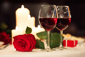 Valentine's Day Background. Two Red Wine Glasses And Rose Lying On Restaurant Table Served For Romantic Date. Selective Focus