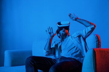 Scared person watching at horror movie by using VR goggles while sitting at sofa. Caucasian man looking at scary video or playing horror games by using virtual reality simulated world. Deviation.