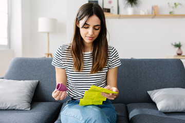 Front view of millennial woman holding eco-friendly silicone menstrual cup while reading use...