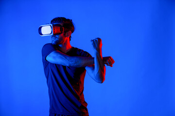 Happy man with VR goggle exercising and stretching arm at neon light background. Caucasian person...