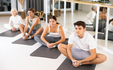 Obraz premium Sporty slender males and females doing exercises on a pilates mat during group training at gym. Healthy lifestyle concept.