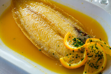 Appetizing black sole fish in orange dipping sauce garnished with orange slices and greens