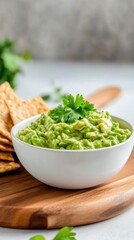 Obraz premium Delicious creamy guacamole served in a bowl with fresh cilantro on a wooden board alongside crispy crackers.