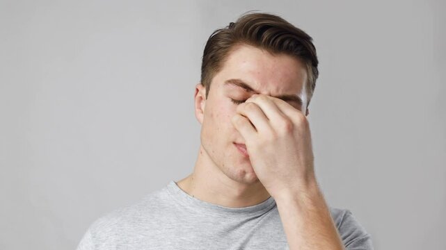 Sinusitis problem. Close up portrait of young sick man rubbing his sore nose, grey studio background, slow motion