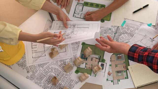 Architect and safety engineer discussion about building construction use blueprint on table with architectural document, measurement tool and wooden block scatter around at modern office. Delineation.