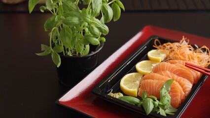Red plate elegance enhances sashimi presentation in restaurant. Fresh fish slices with basil and...