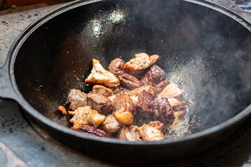 Pieces of lamb with carrots and onions are fried in boiling oil on the fire. preparation of traditional pilaf. cooking pilaf in a cast iron cauldron.