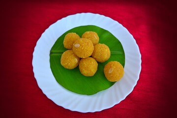 Yellow small ladoo, Indian traditional festive season special sweet on a plate, isolated on red background