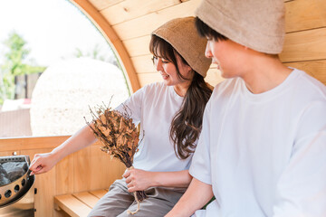 サウナでヴィヒタを使うTシャツ姿のカップルの若い男女
