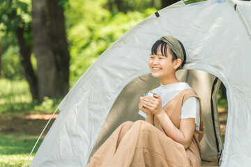 キャンプ場・レジャー施設でテントの前でドリンクを飲む女の子

